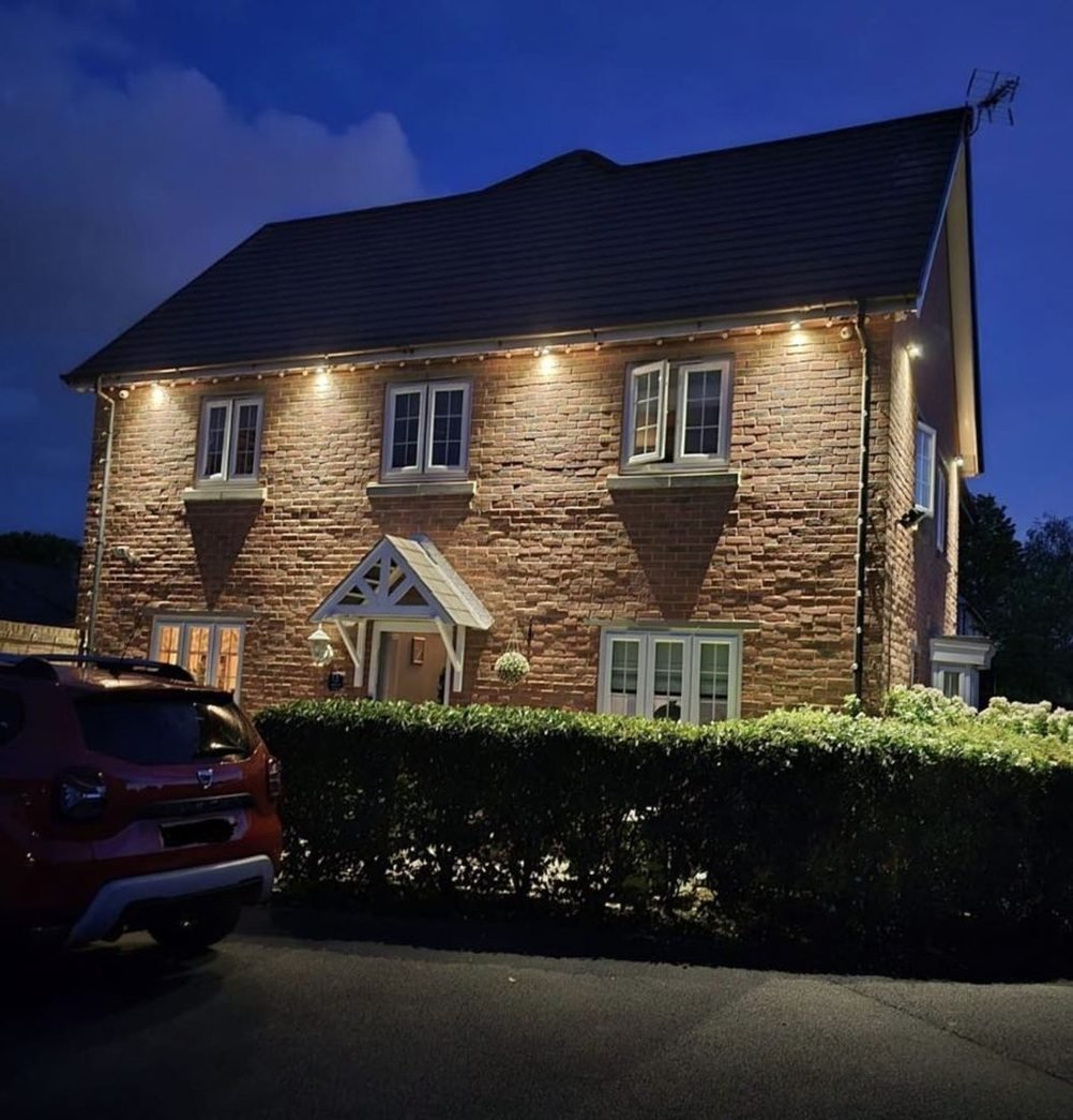 Brick house lit by eaves lights at dusk